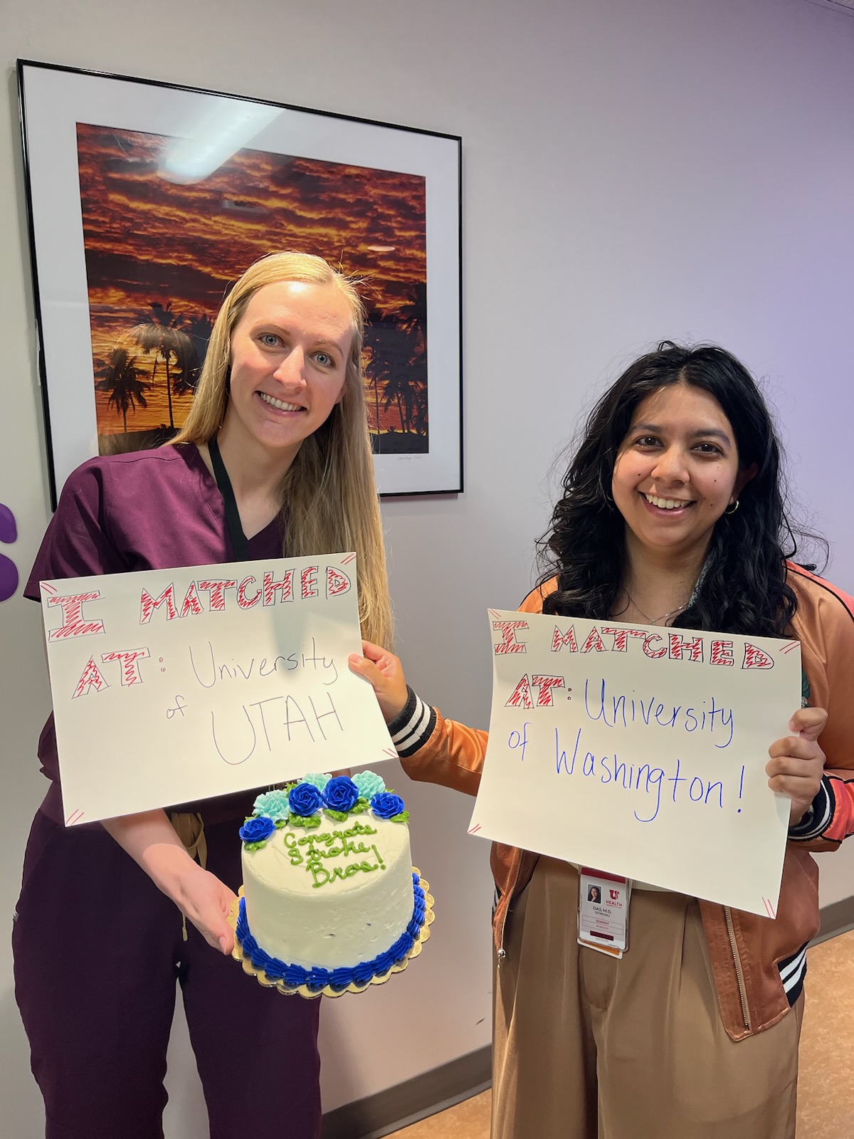 Two people holding matching day posters and a cake
